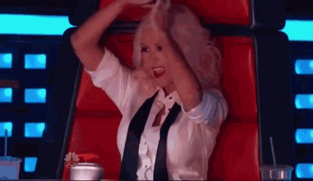a woman in a white shirt and black tie is sitting in a red chair .