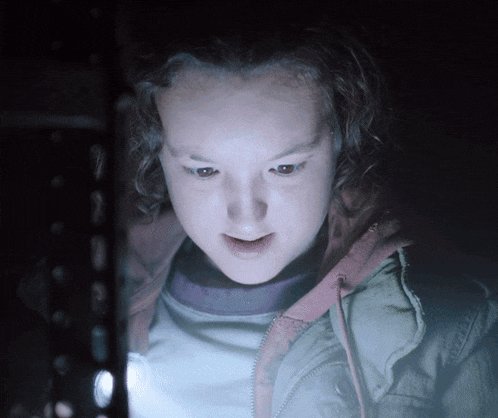 a girl is looking at something in the dark with a light shining on her face