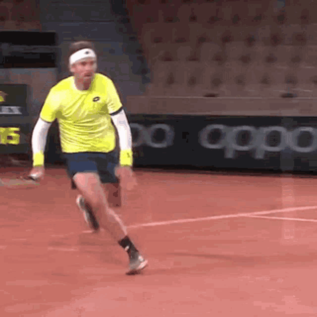 a man in a yellow shirt is running on a tennis court holding a tennis racket .
