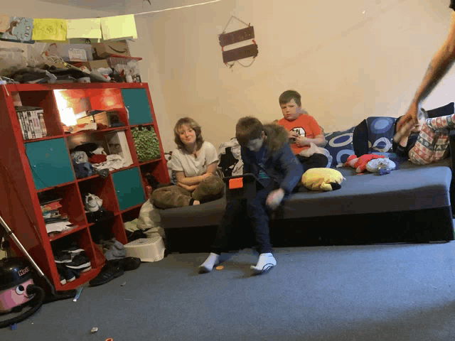 a family sits on a couch in a messy room with a sign on the wall that says " home "
