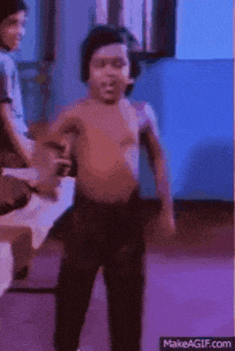 a young boy without a shirt is dancing in a room with other people .