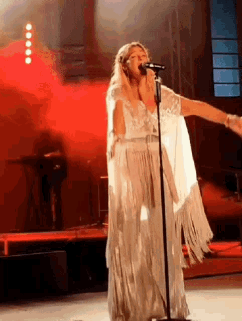 a woman in a white dress singing into a microphone on a stage .