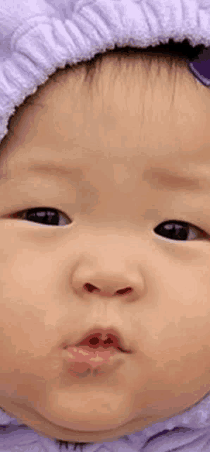 a close up of a baby wearing a purple hat and making a funny face .