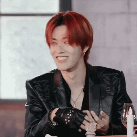 a young man with red hair is sitting at a table wearing a black leather jacket and gloves .