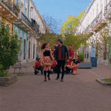 a group of people are walking down a street with a woman in a red skirt