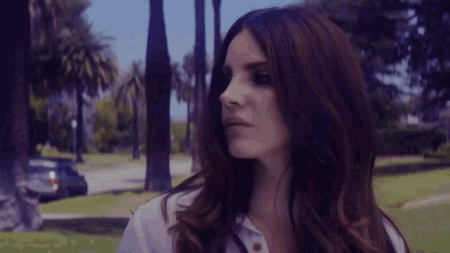 a woman in a white shirt is standing in a park with palm trees in the background