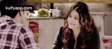 a man and a woman are sitting at a table talking to each other in a kitchen .