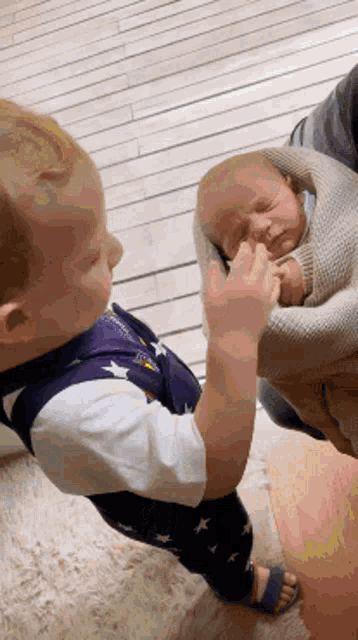 a little boy is holding a baby in his arms and touching it 's face