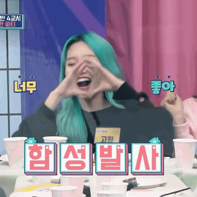 a woman with green hair is making a heart with her hands