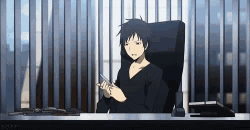 a man in a black shirt is sitting at a desk with a cell phone in his hand