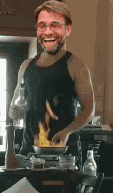 a man in a black tank top smiles while cooking