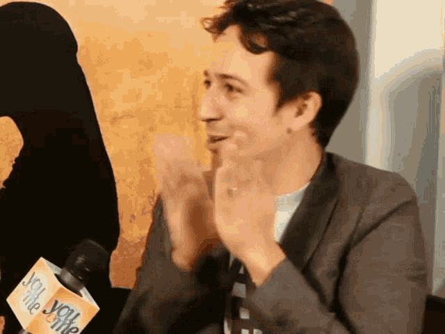 a man in a suit is clapping in front of a microphone that says you like me