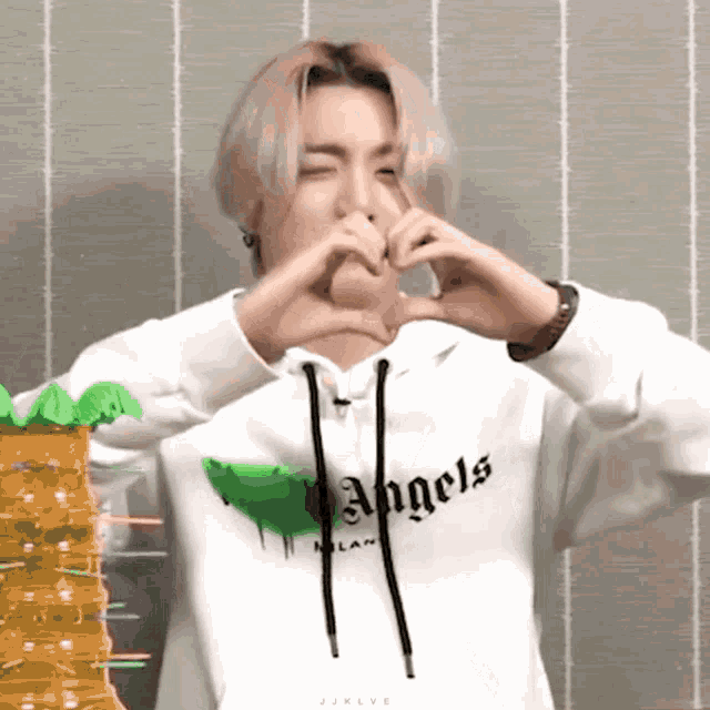 a person wearing a white hoodie with the word angels on it making a heart shape with their hands .