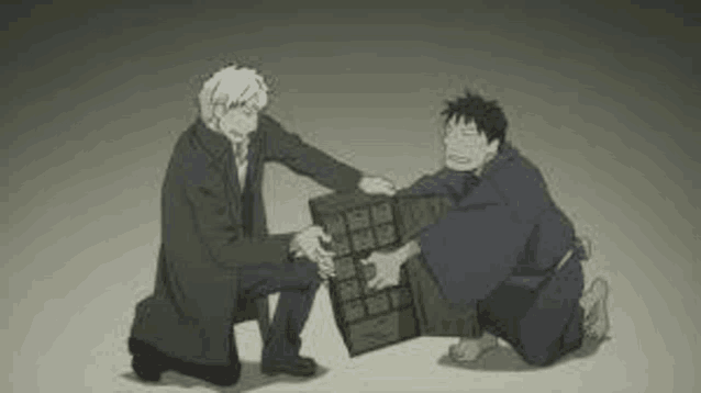 a man in a suit is kneeling down next to another man holding a box .