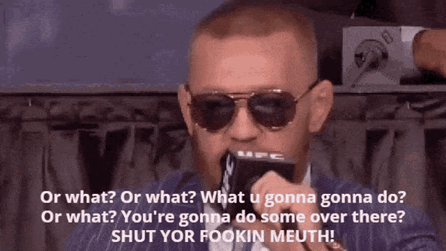 a man wearing sunglasses is talking into a microphone with the words " or what or what what u gonna do "