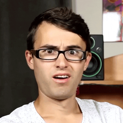 a man wearing glasses making a funny face in front of a green speaker