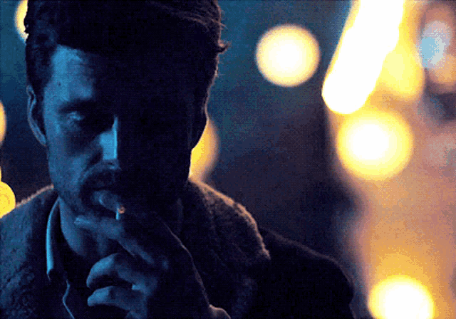 a man smoking a cigarette with a blurry background of lights
