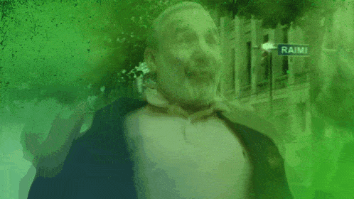 a man with green liquid on his face is standing in front of a street sign that says raimi
