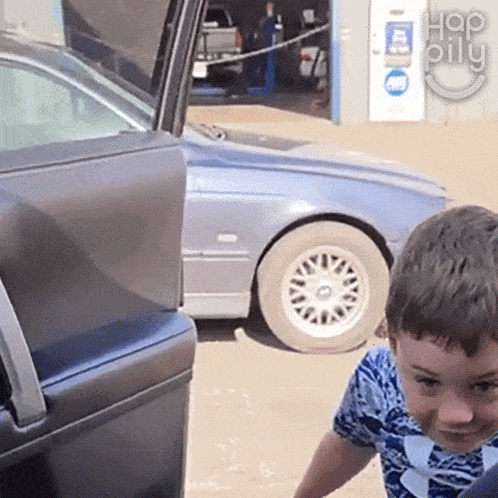 a young boy is standing in front of a car with the word hap on the bottom right
