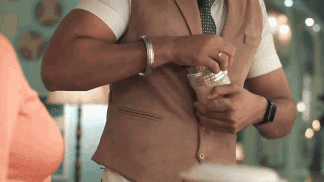 a man wearing a brown vest and tie is holding a jar