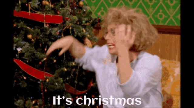 a woman is decorating a christmas tree and the words it 's christmas are visible