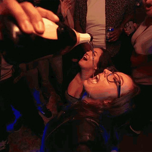 a woman with glasses is pouring a bottle of champagne into her mouth