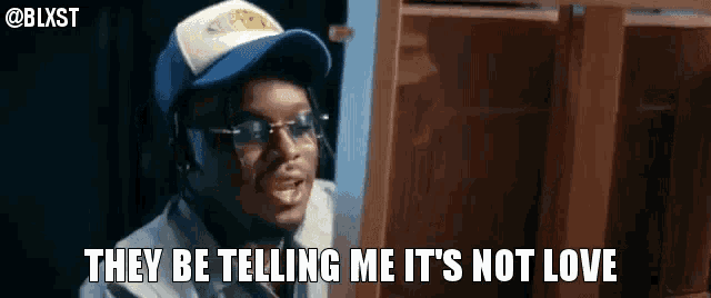 a man wearing a baseball cap and glasses is talking to someone and says they be telling me it 's not love