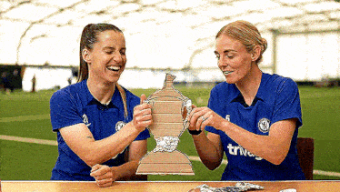 two women are sitting at a table holding a cardboard trophy and smiling .