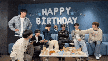 a group of young men are sitting around a table with a happy birthday balloon behind them