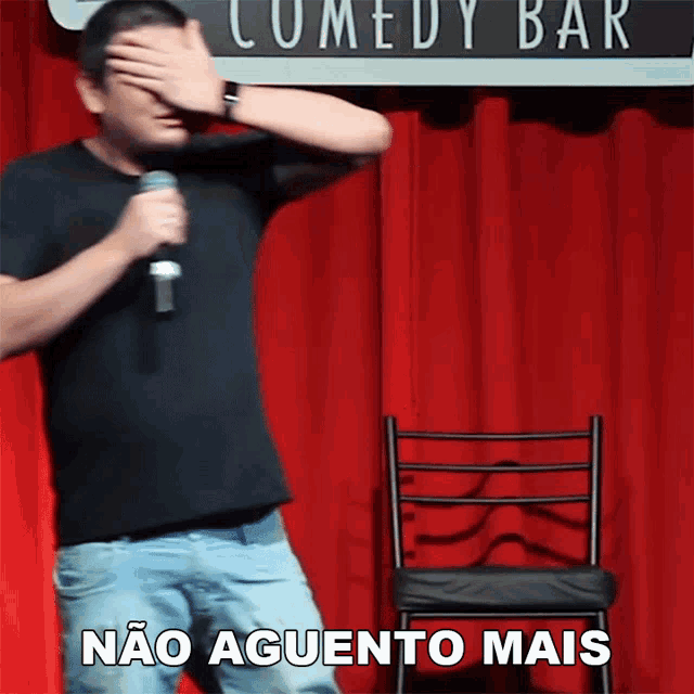 a man covering his face with his hand while holding a microphone in front of a sign that says comedy bar