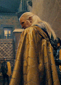 a man with long white hair and a beard is wearing a gold cape .