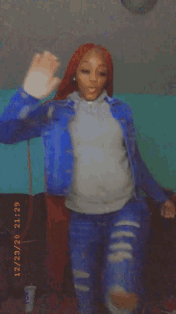 a woman in a blue jacket and ripped jeans is dancing on a bed