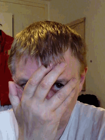a man is covering his face with his hands and looking at the camera