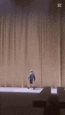a man is walking on a stage in front of a large curtain with the letter m on it .