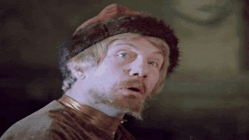 a man with a beard is wearing a fur hat and making a surprised face