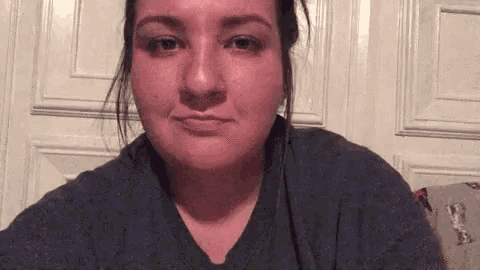 a woman in a gray shirt is making a funny face in front of a door .