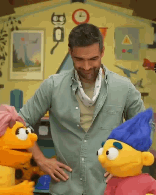 a man in a green shirt is standing next to two stuffed animals one of which has a blue hat on