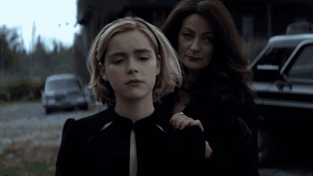 a woman holds a girl 's arm in front of a car