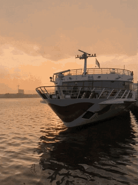 a large white and red boat is docked in the water at sunset