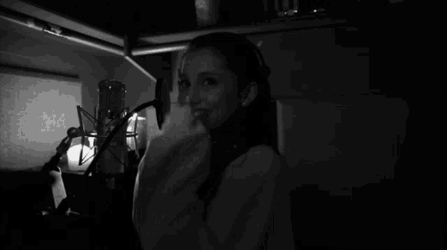 a woman covering her face in front of a microphone in a dark room