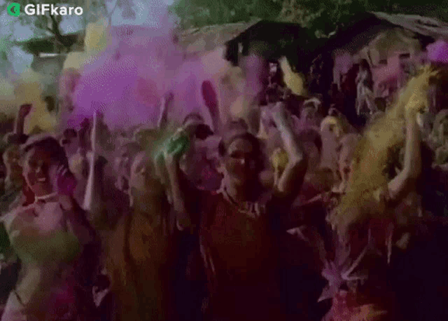 a crowd of people are dancing and throwing colored powder in the air at a party .