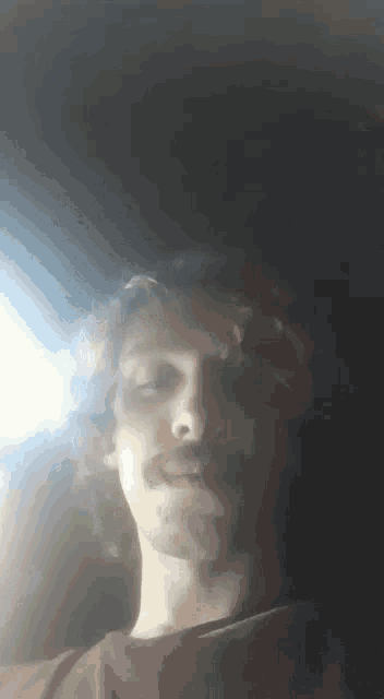 a man with a mustache is looking at the camera in a dark room .