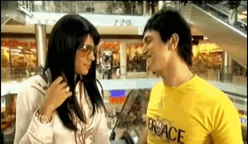 a man wearing a yellow shirt that says versace talks to a woman