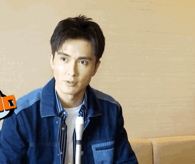 a man in a denim jacket holds a microphone in front of him