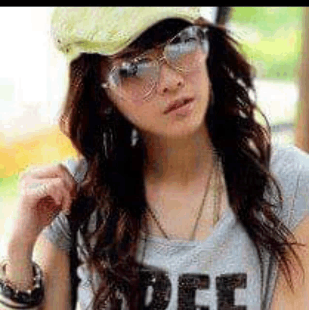 a woman wearing a hat , sunglasses and a t-shirt with the word dee on it is looking at the camera .