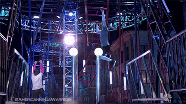 a man is hanging upside down from a ladder in a ninja warrior obstacle course .