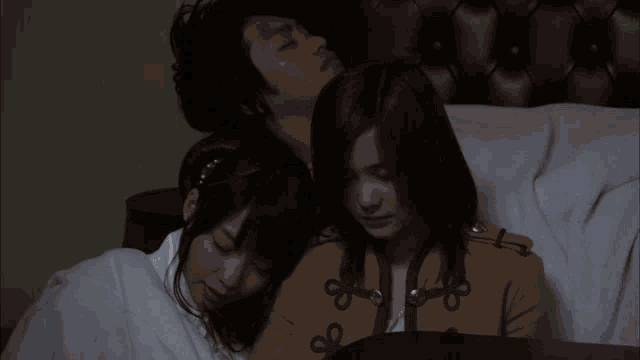 a man and two women are laying on a bed with a white blanket