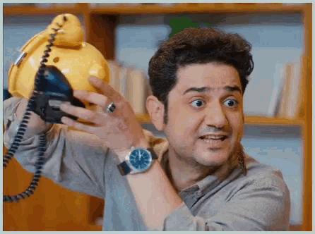 a man wearing a watch holds a yellow telephone in his hand