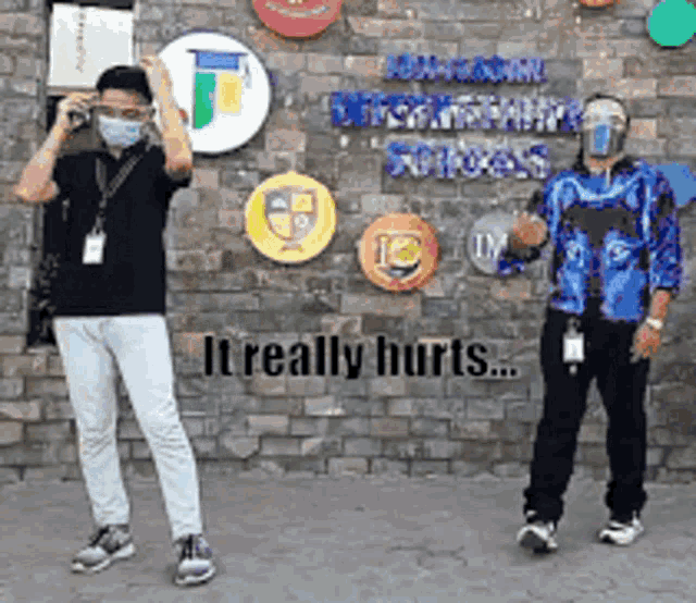 two men wearing face masks are standing in front of a brick wall with the words it really hurts written on it