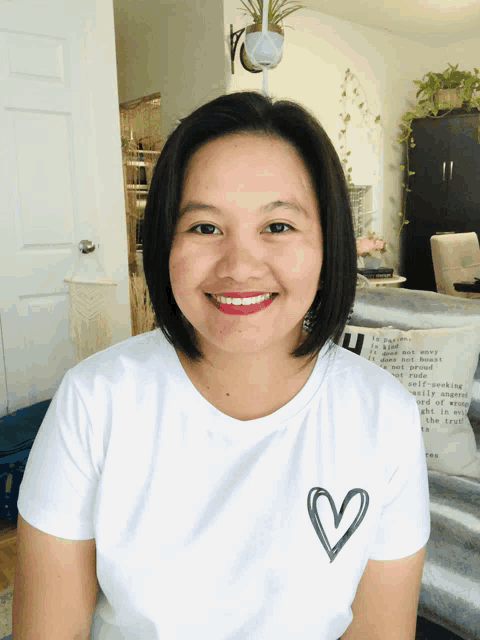 a woman wearing a white shirt with a heart on it smiles for the camera